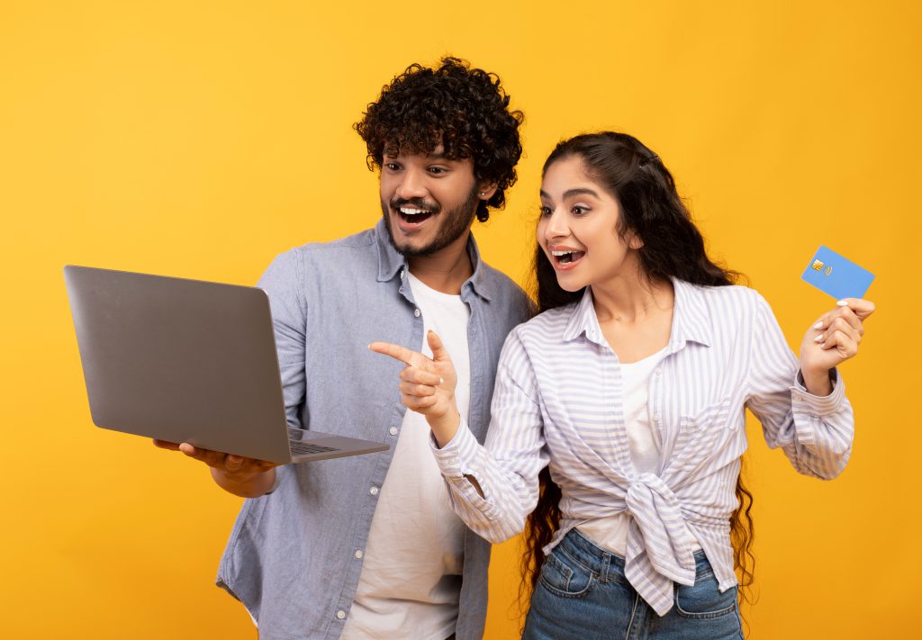 joyful indian couple with credit card and laptop